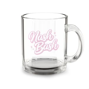 May include: A clear glass mug with a curved handle. The mug features the text "Nash Bash" in a light pink, cursive font with star accents. The mug is empty and sits on a white surface.