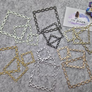 Puede incluir: Una variedad de marcos cuadrados con forma de eslabones de cadena en varios colores metálicos, incluyendo dorado, plateado y negro. Los marcos están dispuestos sobre una superficie gris, con una tarjeta de visita y una flor decorativa en el fondo. Los marcos varían en tamaño.