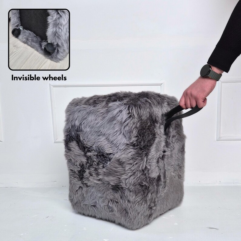May include: A gray, cube-shaped ottoman with a shaggy, faux fur texture. The ottoman has a black handle and sits on invisible wheels. The image includes the text "Invisible wheels".