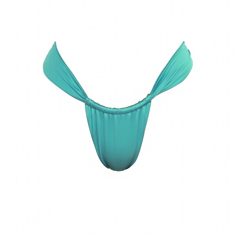 Peut inclure: Bas de maillot de bain de style string turquoise. Le tissu est fronc&eacute; &agrave; l'avant et &agrave; l'arri&egrave;re, avec de longues attaches fluides s'&eacute;tendant sur les c&ocirc;t&eacute;s. Le v&ecirc;tement est fait d'une mati&egrave;re douce et drap&eacute;e.