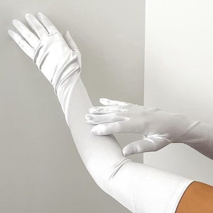 May include: Elegant white satin gloves, extending well past the elbow. The gloves are a bright, solid white, with a smooth, slightly reflective surface. The image shows the gloves on a person's arms, highlighting their length and fit. Perfect for formal events.