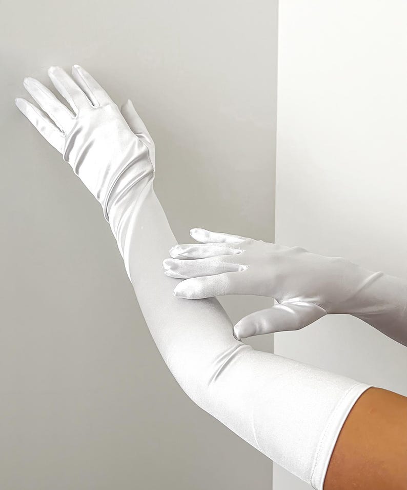 May include: Elegant white satin gloves, extending well past the elbow. The gloves are a bright, solid white, with a smooth, slightly reflective surface. The image shows the gloves on a person's arms, highlighting their length and fit. Perfect for formal events.