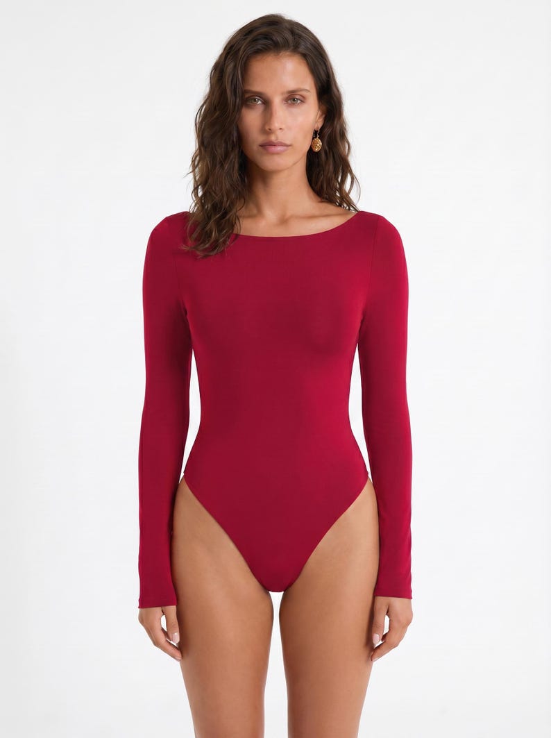 May include: A solid red bodysuit with long sleeves and a scoop neckline. The one-piece garment is form-fitting and made of a smooth, stretchy material. The bodysuit is a deep, rich shade of red.