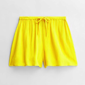 May include: Vibrant yellow shorts with a drawstring waist. The shorts are crafted from a textured material and have a loose fit. The shorts are a solid colour and appear to be lightweight.