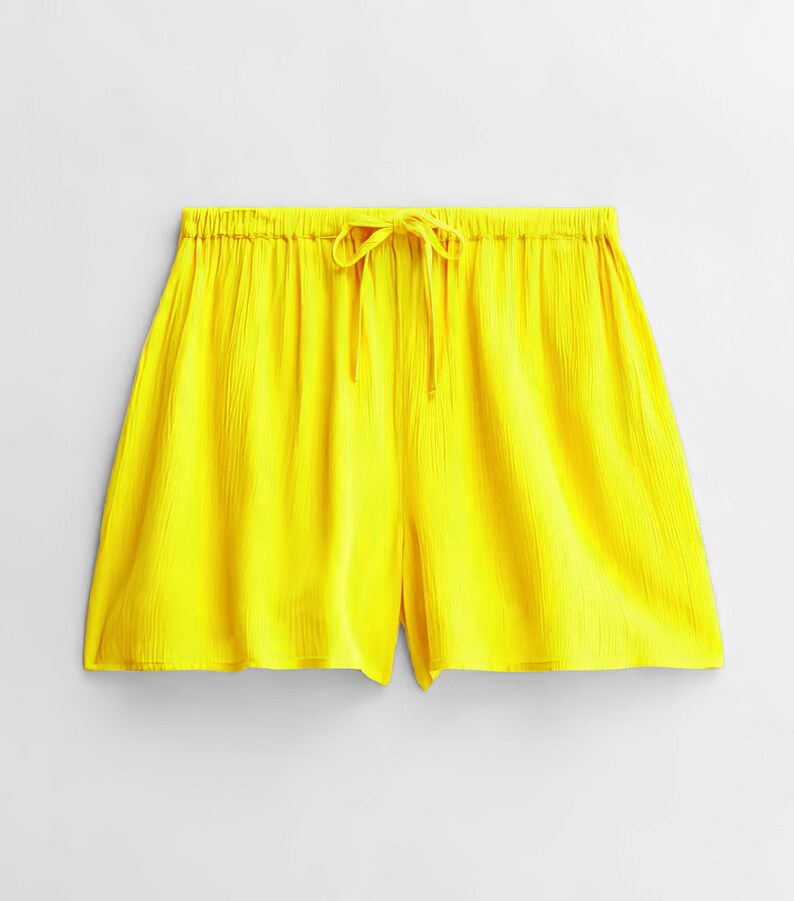May include: Vibrant yellow shorts with a drawstring waist. The shorts are crafted from a textured material and have a loose fit. The shorts are a solid colour and appear to be lightweight.