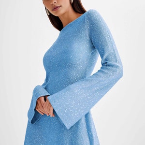 Peut inclure: Robe bleu clair &agrave; manches longues avec un aspect textur&eacute; et &agrave; paillettes. La robe pr&eacute;sente une encolure bateau et des manches &eacute;vas&eacute;es. Le v&ecirc;tement est de longueur genou et a une silhouette ajust&eacute;e.
