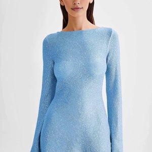 Peut inclure: Une robe bleu clair &agrave; manches longues avec un col bateau. La robe a un aspect textur&eacute; et scintillant, refl&eacute;tant la lumi&egrave;re. Le tissu semble &ecirc;tre un mat&eacute;riau tricot&eacute; ou tiss&eacute;. La robe est moulante et arrive &agrave; mi-cuisse.