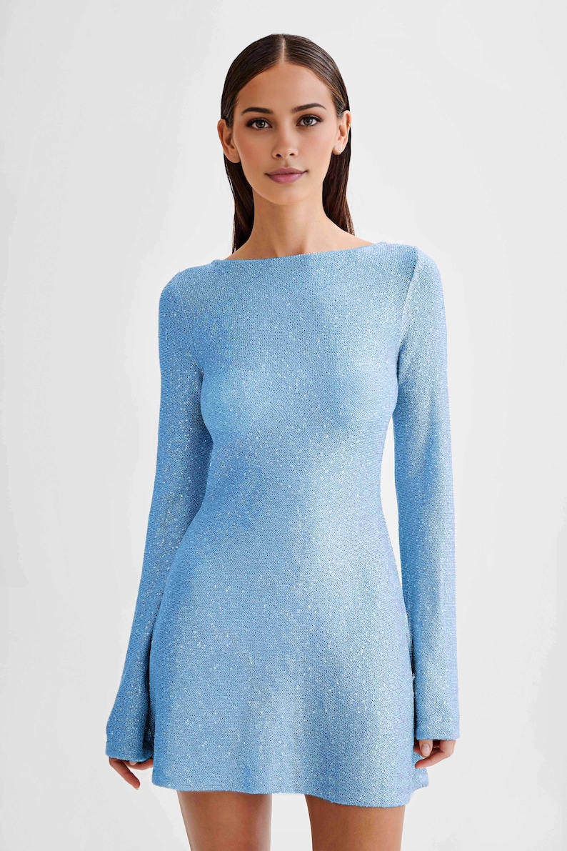 Peut inclure: Une robe bleu clair &agrave; manches longues avec un col bateau. La robe a un aspect textur&eacute; et scintillant, refl&eacute;tant la lumi&egrave;re. Le tissu semble &ecirc;tre un mat&eacute;riau tricot&eacute; ou tiss&eacute;. La robe est moulante et arrive &agrave; mi-cuisse.