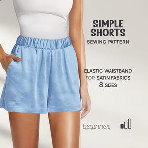 May include: Light blue satin shorts with an elastic waistband. The image includes text that reads "SIMPLE SHORTS SEWING PATTERN" and "ELASTIC WAISTBAND FOR SATIN FABRICS 8 SIZES". The shorts have pockets and are designed for beginners.