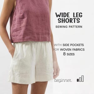 May include: A person wearing a mauve sleeveless top and cream-colored wide-leg shorts. The shorts have side pockets and an elastic waistband. Text on the image reads "WIDE LEG SHORTS SEWING PATTERN" and "WITH SIDE POCKETS FOR WOVEN FABRICS 8 SIZES".