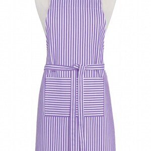 May include: A purple and white striped apron with a neck strap and waist tie. The apron has two front pockets and is displayed on a mannequin. The apron is made of a lightweight fabric.