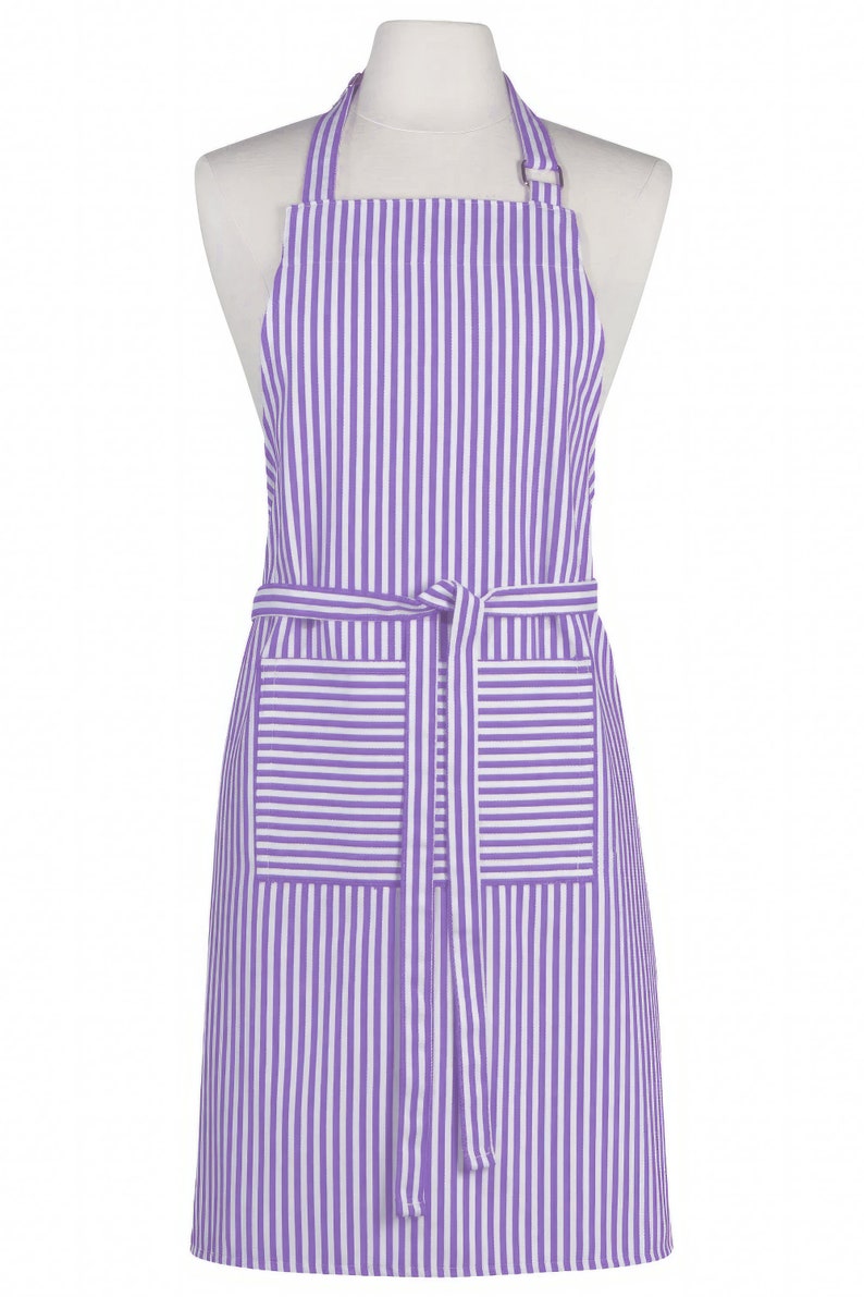 May include: A purple and white striped apron with a neck strap and waist tie. The apron has two front pockets and is displayed on a mannequin. The apron is made of a lightweight fabric.