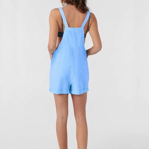 May include: Pale blue romper with adjustable straps and rolled hems. The casual all-in-one garment has a relaxed fit and pockets. The romper is made of a lightweight fabric, ideal for warmer weather.