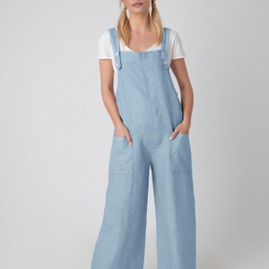 May include: Pale blue linen jumpsuit with wide legs and large front pockets. The jumpsuit features adjustable straps with button fastenings and is worn over a white t-shirt. The model is wearing brown sandals.