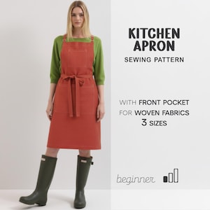 May include: A terracotta-coloured kitchen apron with a front pocket and tie-waist is shown. The apron is part of a sewing pattern for woven fabrics, with the text "Kitchen Apron Sewing Pattern" and "3 Sizes". The model is wearing green boots and a green top.