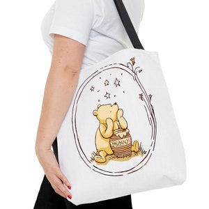 May include: White canvas tote bag with a black strap featuring a cartoon illustration of Winnie the Pooh looking up at stars with a pot of honey that says "Hunny".