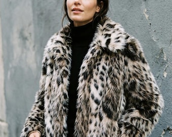 May include: A long-sleeved jacket featuring a faux fur texture with a black and beige leopard print pattern, a wide collar, and a straight hemline, worn over a solid black high-neck sweater.