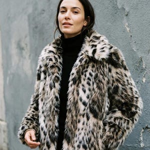 May include: A long-sleeved jacket featuring a faux fur texture with a black and beige leopard print pattern, a wide collar, and a straight hemline, worn over a solid black high-neck jumper.