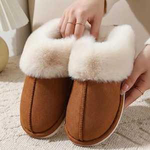 Peut inclure: Une paire de pantoufles en daim marron avec une bordure en fausse fourrure cr&egrave;me. Les pantoufles ont un bout arrondi et une semelle blanche. L'image met en &eacute;vidence la texture douce et le design confortable des pantoufles.