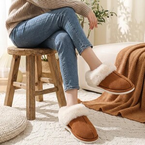 Peut inclure: Pantoufles en daim marron avec une bordure en fausse fourrure blanche. Les pantoufles ont un design &agrave; enfiler avec une semelle blanche. L'image sugg&egrave;re confort et chaleur. Les pantoufles sont de couleur neutre, adapt&eacute;es &agrave; diverses tenues.