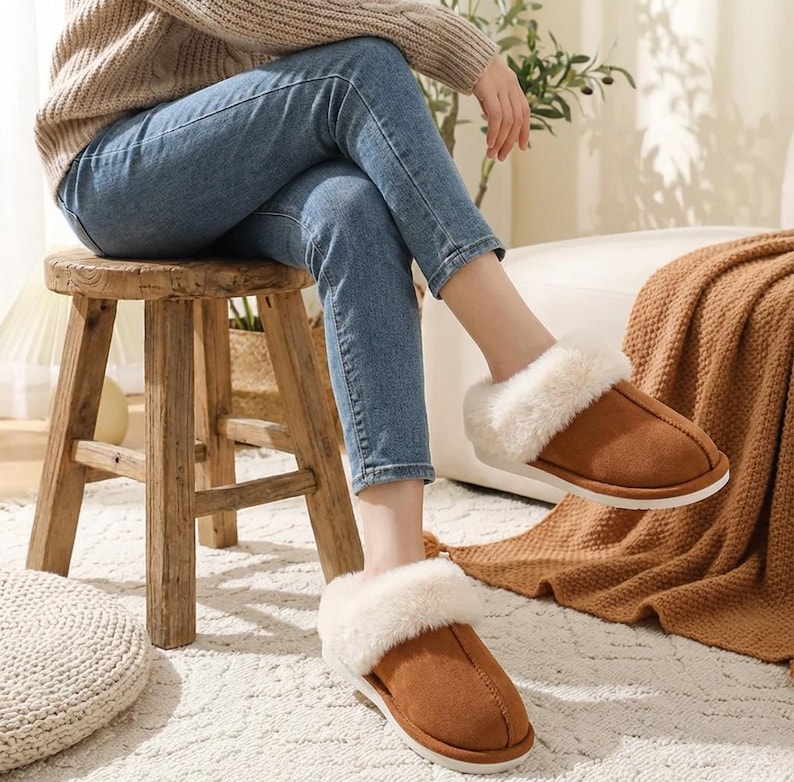 Peut inclure: Pantoufles en daim marron avec une bordure en fausse fourrure blanche. Les pantoufles ont un design &agrave; enfiler avec une semelle blanche. L'image sugg&egrave;re confort et chaleur. Les pantoufles sont de couleur neutre, adapt&eacute;es &agrave; diverses tenues.