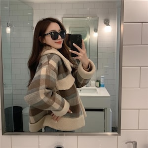 May include: A brown and beige checked jacket with a cream-coloured shearling collar and trim. The jacket has long sleeves and is being worn in front of a mirror. A stylish outerwear garment.