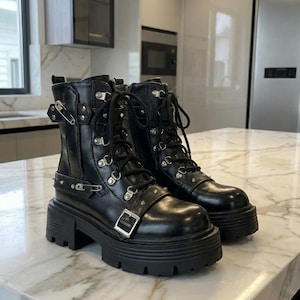 May include: A pair of black leather boots with a chunky platform sole. The boots feature multiple silver-tone buckles, grommets, and laces. The boots are approximately 6 inches tall.
