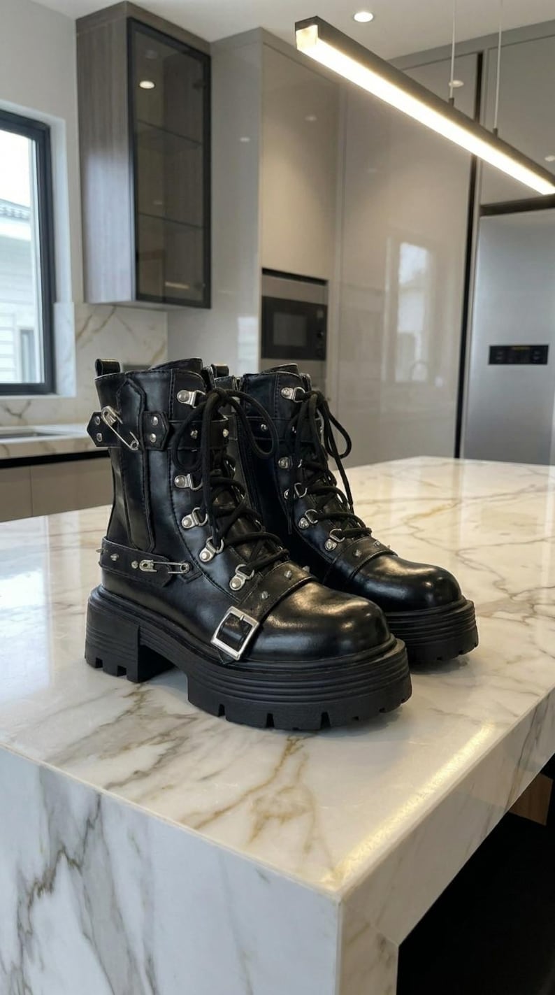 May include: A pair of black leather boots with a chunky platform sole. The boots feature multiple silver-tone buckles, grommets, and laces. The boots are approximately 6 inches tall.