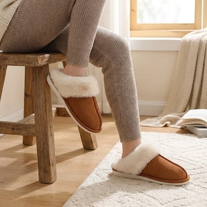 Peut inclure: Pantoufles en daim marron avec une bordure en fausse fourrure cr&egrave;me. Les pantoufles sont pr&eacute;sent&eacute;es sur les pieds d'une personne, pos&eacute;es sur un tapis cr&egrave;me. Les pantoufles ont un aspect doux et confortable.