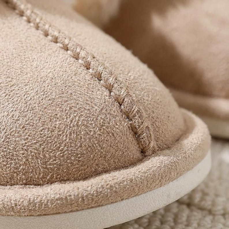 Peut inclure: Gros plan sur une pantoufle beige avec un ext&eacute;rieur textur&eacute; semblable &agrave; du daim. La pantoufle pr&eacute;sente un d&eacute;tail de couture et une semelle blanche. L'accent est mis sur la mati&egrave;re douce et confortable.