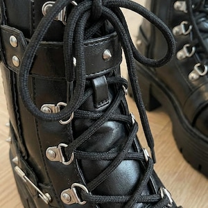 May include: Black leather boots with silver-tone hardware, including studs and buckles. The boots feature a lace-up design with thick black laces and a chunky platform sole. The boots have a gothic or punk aesthetic.