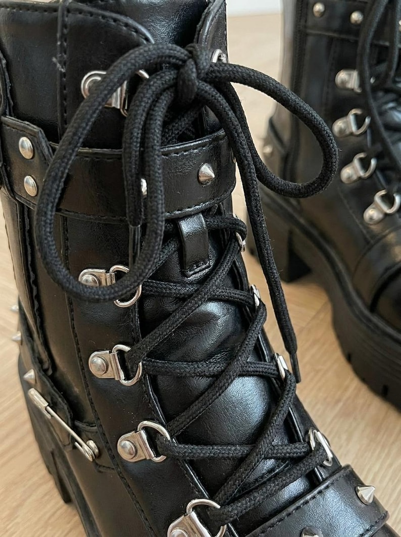 May include: Black leather boots with silver-tone hardware, including studs and buckles. The boots feature a lace-up design with thick black laces and a chunky platform sole. The boots have a gothic or punk aesthetic.