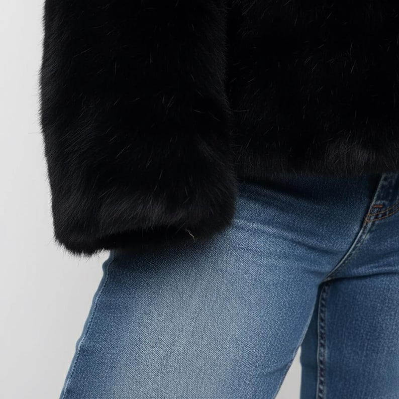 May include: A close-up of a black faux fur jacket sleeve and light blue denim jeans. The jacket's fur appears soft and plush. The jeans are a classic blue wash.