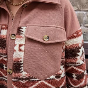 May include: A dusty rose jacket with a textured weave and a collared neckline. The jacket features two front pockets and button closures. The sleeves have a patterned design in shades of brown, cream, and rust.