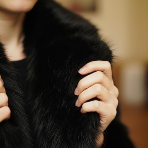 May include: Close-up of a black fur coat with a plush, textured appearance. The coat's collar is prominent, and the fur appears soft and luxurious. The image highlights the coat's rich color and texture.