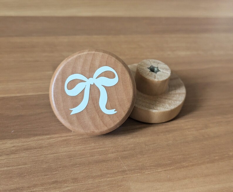 Peut inclure: Deux boutons de meuble en bois. L'un pr&eacute;sente un motif de n&oelig;ud bleu clair sur une surface ronde et marron clair. Le second est marron clair avec une base cylindrique et un dessus rond. Les boutons sont en bois.