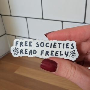 May include: A white ceramic mug with a black handle and the text "But first, coffee" in a handwritten style. The mug is on a white surface. The mug is approximately 4 inches tall.