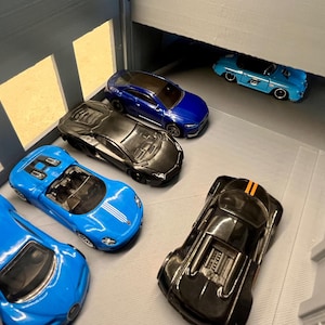 May include: A collection of toy cars in various colors, including blue and black, are arranged in a miniature garage setting. The cars have detailed features, such as headlights and racing stripes.
