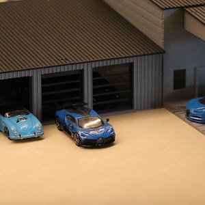 May include: Miniature blue sports cars parked in and around a model garage. The garage has three bays, with two cars inside and one parked outside. The cars are various shades of blue.