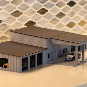 May include: A miniature model of a modern garage or auto shop. The building has a gray exterior with a dark brown roof. A small silver car is parked under a covered area. Several colorful toy cars are visible inside the garage.
