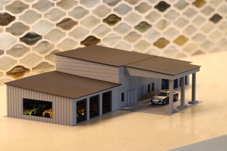 May include: A miniature model of a modern garage or auto shop. The building has a gray exterior with a dark brown roof. A small silver car is parked under a covered area. Several colorful toy cars are visible inside the garage.