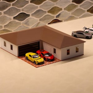 May include: A miniature garage model with a brown roof and white walls. Several toy cars in yellow, red, gray, white, and green are parked in front of the garage and on the side. The garage door is black.