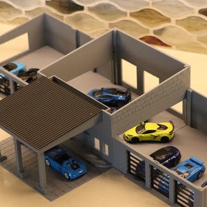 May include: A gray miniature garage structure with a brown roof, housing several toy cars in various colors, including blue and yellow. The model has open bays and a carport, designed for toy car display.