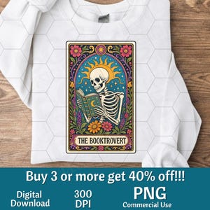 Puede incluir: Una sudadera blanca de manga larga con un gráfico rectangular de un esqueleto leyendo un libro bajo un sol y estrellas. El diseño incluye bordes florales coloridos y el texto THE BOOKTROVERT impreso en una cinta inferior.