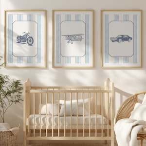 May include: Three framed prints with vintage vehicle illustrations: a motorcycle, airplane, and car. Each print has a blue and white striped background and a light wood frame. A light wood crib, wicker chair, and round rug complete the nursery scene.