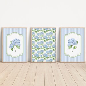 May include: Three framed art prints featuring blue hydrangea flowers. Two prints have a blue and white striped background with a floral design in a white and green frame. The third print has a repeating hydrangea pattern.