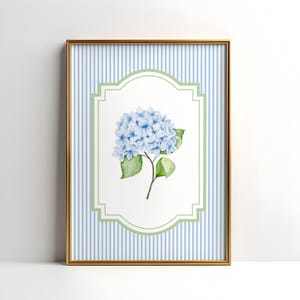 May include: A framed print with a watercolour illustration of a blue hydrangea flower. The artwork is set against a background of blue and white vertical stripes, framed by a gold border. The hydrangea is in a white and green decorative frame.