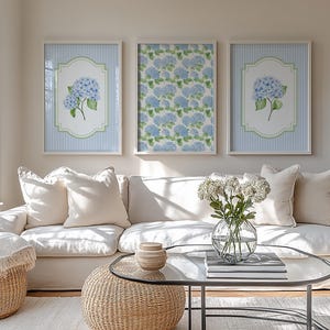 May include: Three framed wall art pieces with blue hydrangea floral prints. Two prints have a blue and white striped background with a floral design in a white and green frame. The third print has a blue floral pattern.