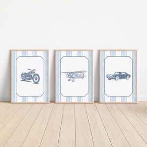 May include: Three framed prints featuring vintage vehicles: a motorcycle, a biplane, and a classic car. Each print has a blue and white striped border and a light wood frame. The illustrations are in shades of blue.