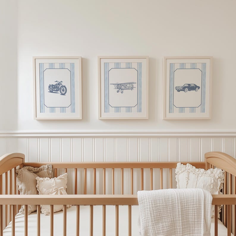 May include: Three framed prints with blue and white striped backgrounds. Each print features a different vehicle: a motorcycle, a biplane, and a car. The frames are light-colored wood, and the prints are displayed above a wooden crib.